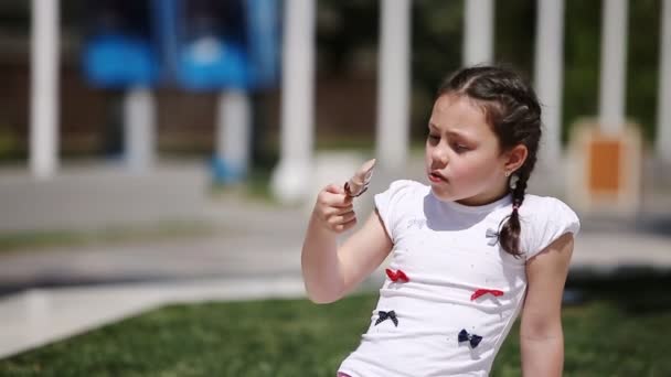 Милая девушка ест коричневое мороженое в парке в летний солнечный день . — стоковое видео