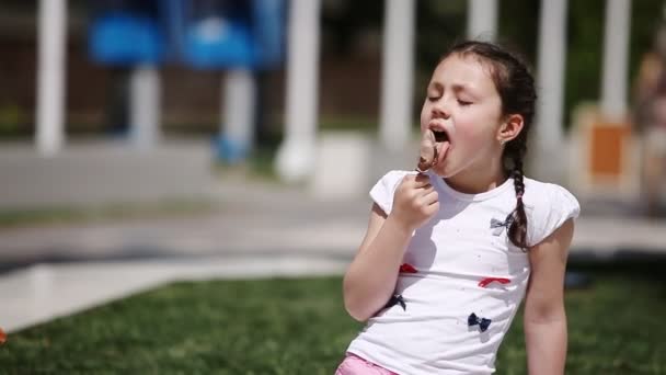 Ragazza carina mangiare gelato marrone nel parco nel giorno di sole estivo . — Video Stock