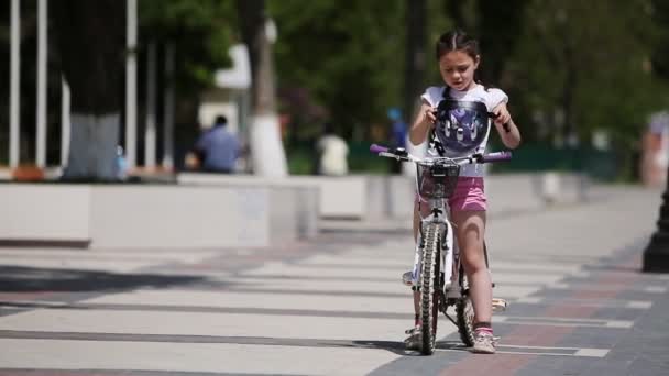 Menina bonito usando capacete e, em seguida, monta uma bicicleta no parque em dia de sol . — Vídeo de Stock