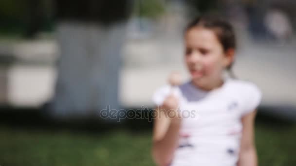 Gros plan de mignonne petite fille mangeant de la crème glacée dans le parc au soleil jour d'été . — Video