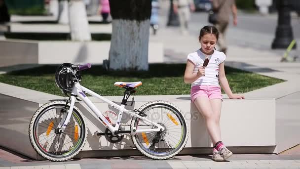 Petite fille mignonne mangeant de la crème glacée dans le parc de la ville au soleil jour d'été . — Video