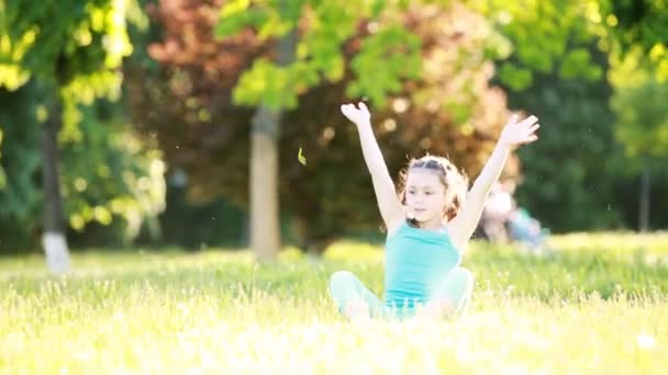 Милая маленькая девочка, сидящая на лугу и играющая в парке в летний день . — стоковое видео