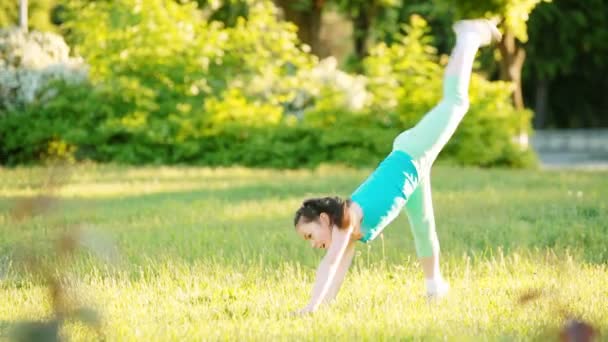 Sportig liten flicka gör en cartwheel på ängen i parken sommaren. — Stockvideo