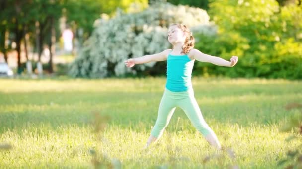 Petite fille sportive faisant une roue sur la prairie dans le parc d'été . — Video