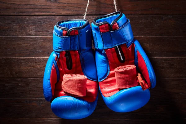 Blue and red boxing gloves and bandage on brown plank background.