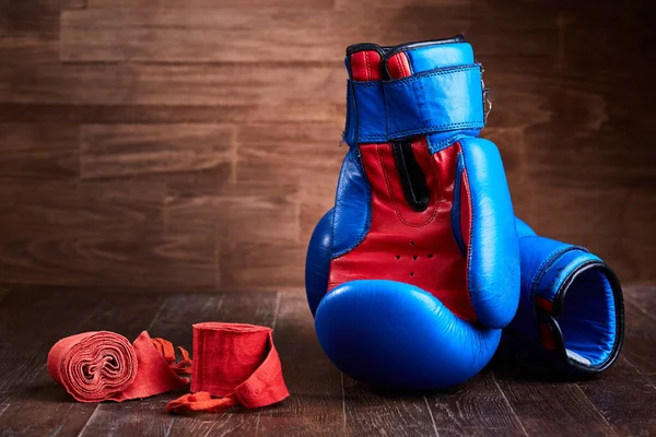Pair of red and blue boxing gloves and red bandage on brown plank.