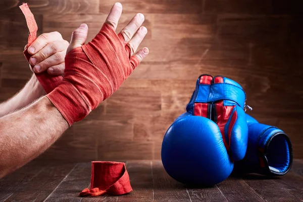 Спортивный человек заворачивает руки бинтами и боксерскими перчатками на деревянной доске . — стоковое фото