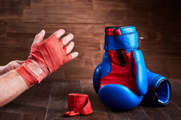 Sprawny człowiek Zawijanie jego ręce bandaż i rękawice bokserskie na drewniane deski. — Zdjęcie stockowe