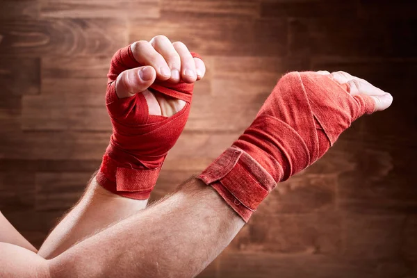 Close-up of the muscular mans hands with red bandage against wooden wall.