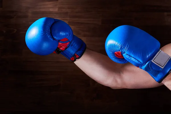 Niebieskie i czerwone rękawice bokserskie na ręce na brązowym tle. — Zdjęcie stockowe