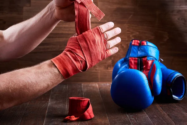 Спортивный человек заворачивает руки бинтами и боксерскими перчатками на деревянной доске . — стоковое фото