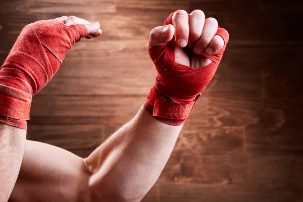 Close-up das mãos dos homens musculares com bandagem vermelha contra a parede de madeira . — Fotografia de Stock