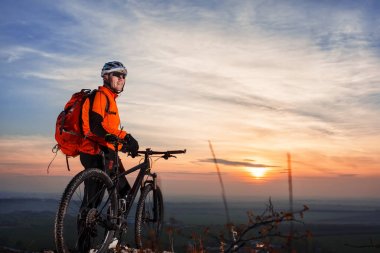 Bisikletçi bisiklet günbatımı görünümünü doğal manzarası önünde karşı yaslanmış.