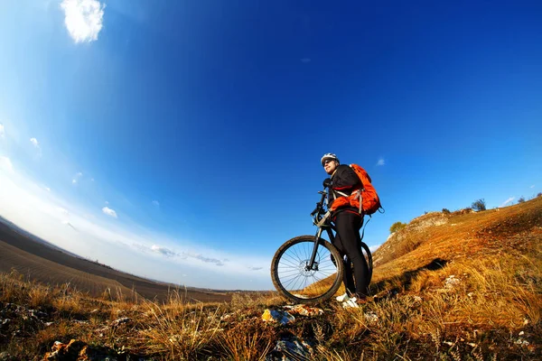 Nízký, široký úhel portrét proti modré obloze horských biker jízdě z kopce. Cyklista v černé sportovní vybavení a helmu — Stock fotografie