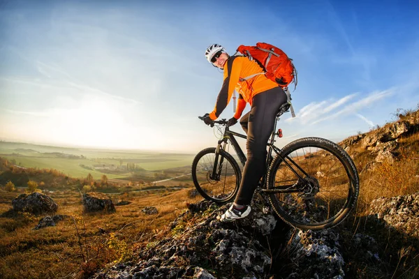Cyclist in helmet and glasses on mountain bike stands on the precipice of hill under blue sky and sun. Wide angle view — Stock Photo, Image