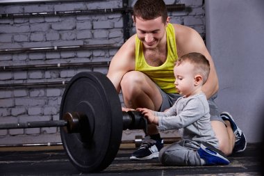 Halter küçük oğlu için gösterilen ve haç tuğla duvara gülümseyen genç sportif babası uygun spor salonu.