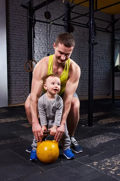 Mutlu baba ve dumbell ile egzersiz ve tuğla duvara gülümseyen küçük şirin oğlu.