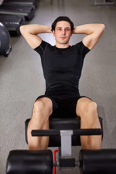 Junger Sportler in schwarzer Sportbekleidung macht im Fitnessstudio Bauchübungen. — Stockfoto