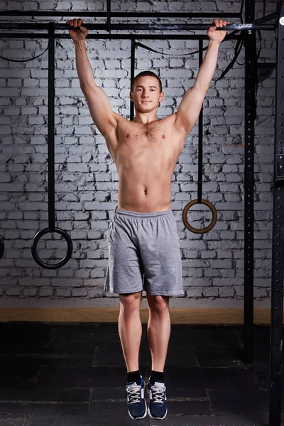 Junger muskulöser Mann macht Übungen am Reck in einem Turnverein gegen Ziegelwand. — Stockfoto