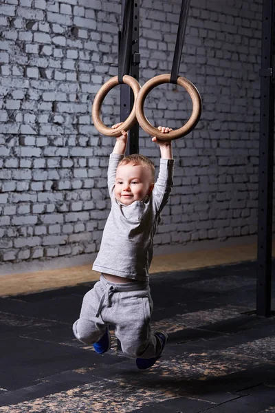 Симпатичный мальчик висит на гимнастических кольцах в кресте прилегает спортзал к кирпичной стене . — стоковое фото