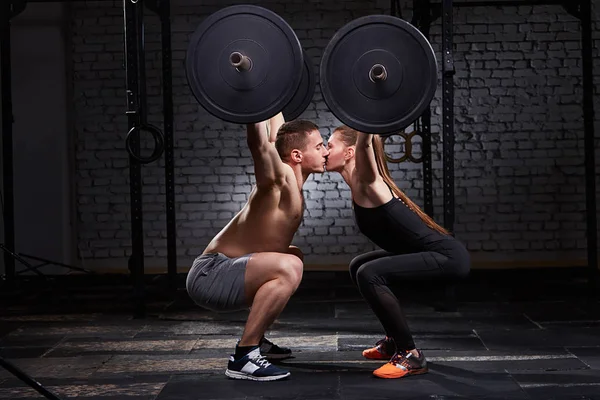 Genç güzel sportif kadın ve erkek öpüşme ve spor salonunda ağız kavgası tuğla duvarın üzerinden bir halter kaldırma.