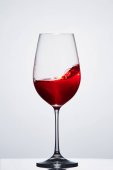 Červené víno v křišťálové čisté sklenici ukazující vlny proti světlé pozadí.