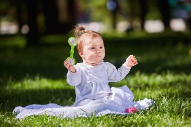 Sıcak yaz gününde Şehir Parkı yeşil çimlere oturup şirin bebek kız.