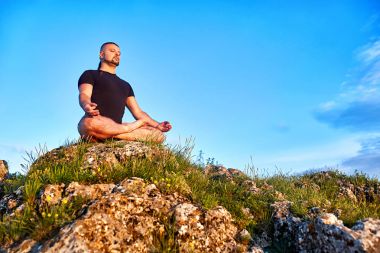 Mavi Gökyüzü bulutlu lotus konumunda bir kayaya oturan genç adam.