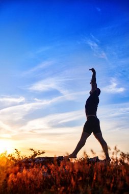 Yoga çayır üzerinde günbatımında kırsal kesimde yaparken genç adam silüeti.