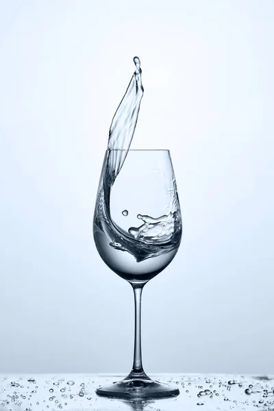 Glass of cool cleaner splashing water while standing on the glass with water bubbles against light background.