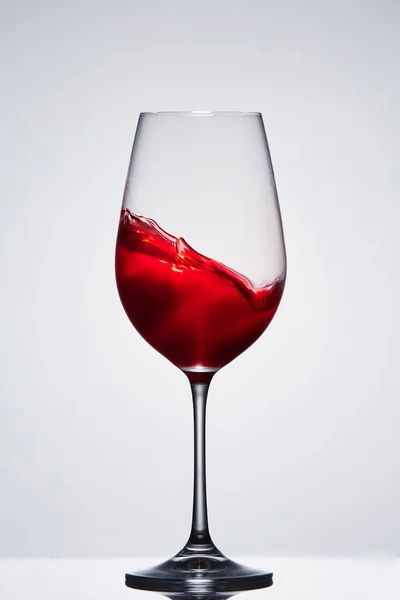 Движущееся красное вино в элегантном бокале, стоящем на светлом фоне с отражением . — стоковое фото