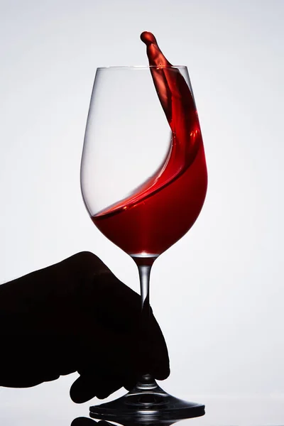 Рука держит чистый бокал с брызгами красного вина стоя на фоне света . — стоковое фото