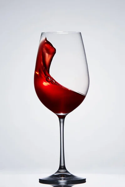 Pohybující se na červené víno v čistě křehkou skleničku stojící proti světlé pozadí s odleskem. — Stock fotografie