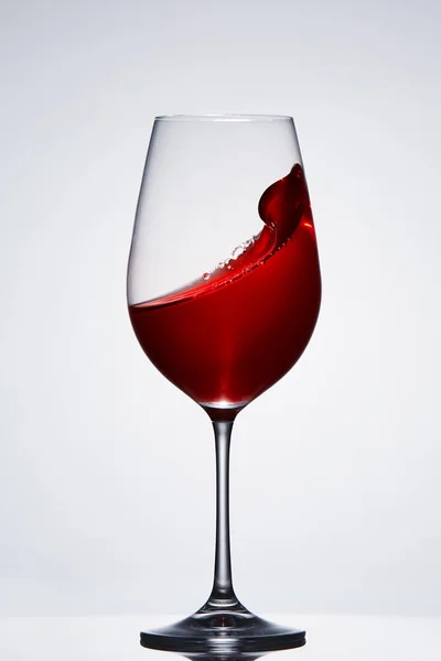Разбрызгивание и перемещение красного вина в чистом бокале, стоящем на светлом фоне с отражением на подставке . — стоковое фото