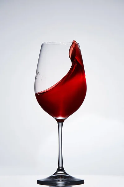 Elegantní čistou sklenici s vlnou zářivě červeného vína stojící proti světlé pozadí s odleskem dole. — Stock fotografie