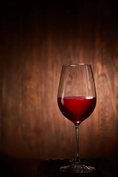 Verre à vin rouge à moitié plein et fragile, debout sur un fond en bois . — Photo