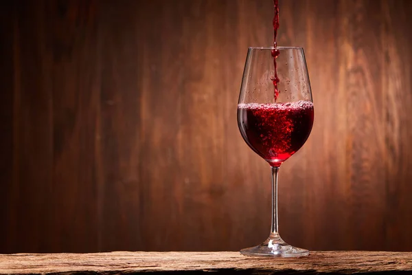 Vin rouge savoureux versé dans l'élégant verre debout sur le support en bois sur fond de mur en bois . — Photo