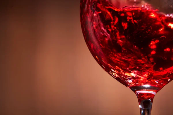 Gros plan sur les éclaboussures abstraites du vin rouge dans le verre à vin fragile sur le fond brun en bois . — Photo