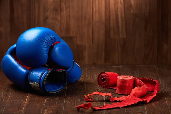 Par de guantes de boxeo azul con dos rollos de vendaje manual sobre fondo de madera . — Foto de Stock