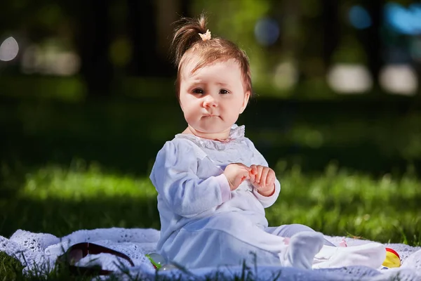 Niña en vestido de verano sentada en el prado verde en el parque de la ciudad . — Foto de Stock