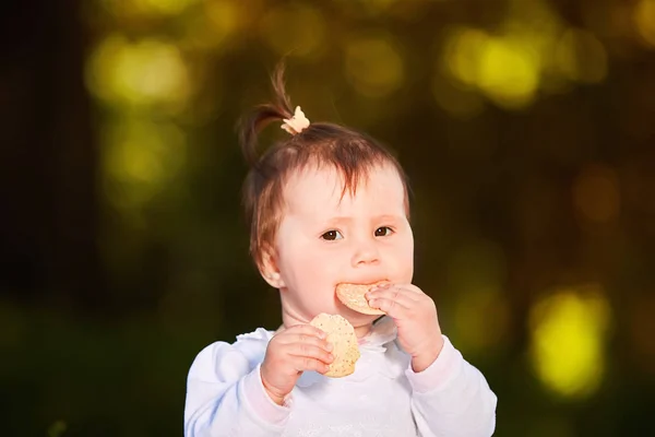 Close-up van schattige babymeisje zit in het park en de snack op warme dag eet. — Stockfoto