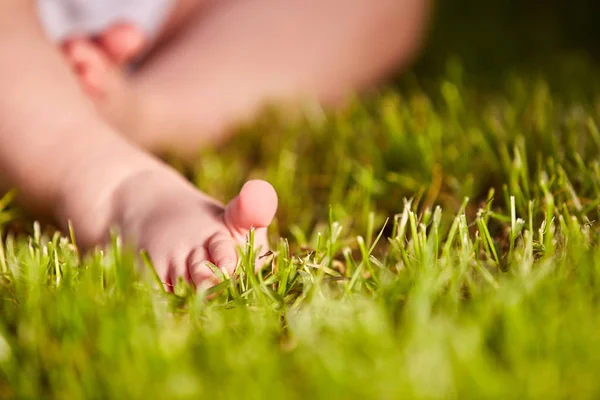 Primer plano de los pequeños pies de bebé sobre hierba verde al aire libre en el parque de la ciudad . — Foto de Stock