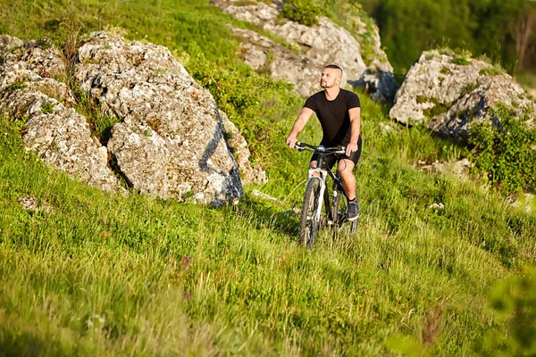 Привлекательный велосипедист катается на велосипеде по лугу с камнями в сельской местности . — стоковое фото