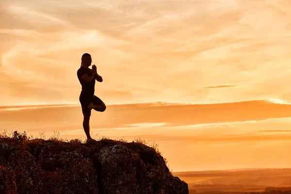Silueta del hombre practicando yoga en la colina contra el hermoso atardecer . —  Fotos de Stock