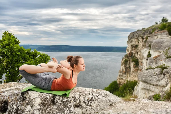 Sportive woman practicing yoga on the rock against beautiful landscape.