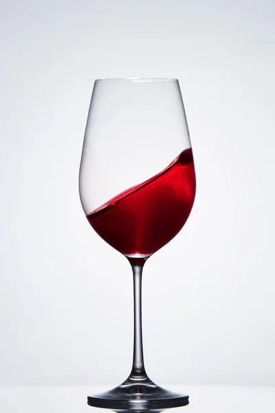 Moving red wine in the pure fragile wineglass standing against light background with reflection. — Stock Photo, Image