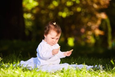 Yaz günü Şehir Parkı yeşil çimenlerin üzerinde oturan neşeli bebek kız.