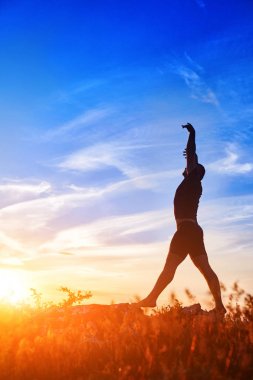 Yoga çayır üzerinde günbatımında kırsal kesimde yaparken genç adam silüeti.