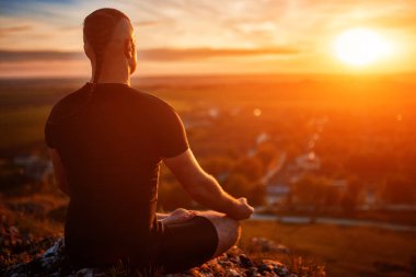 Bir kaya üzerinde lotus poz batımında yoga meditasyon adam arkadan görünüş.