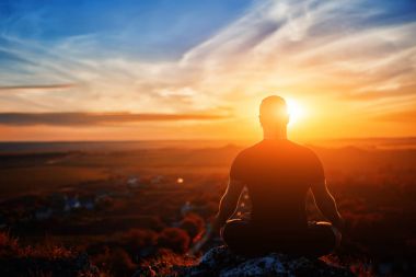 Bir kaya üzerinde lotus poz batımında yoga meditasyon adam arkadan görünüş.